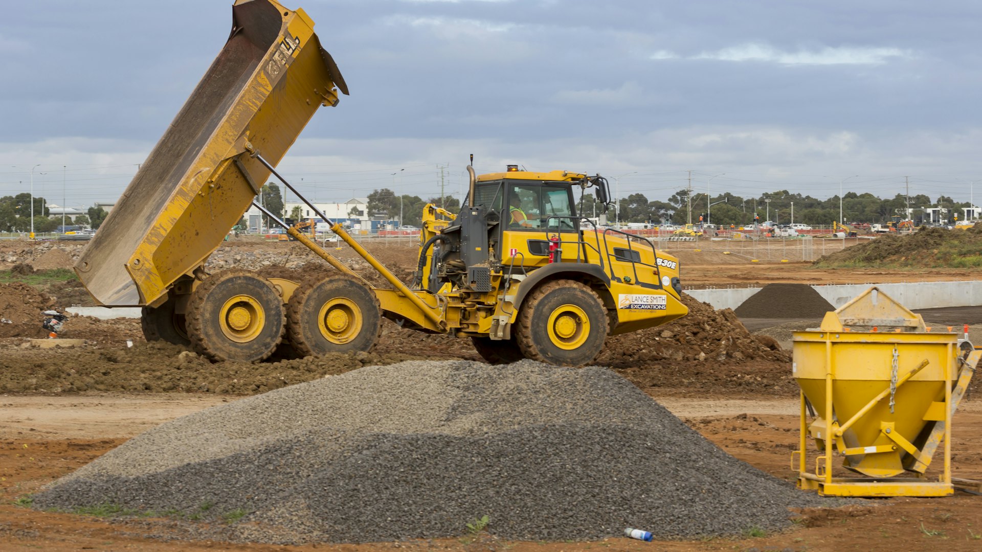 A wheeled loader moving earth across an open worksite under a bright sky.
