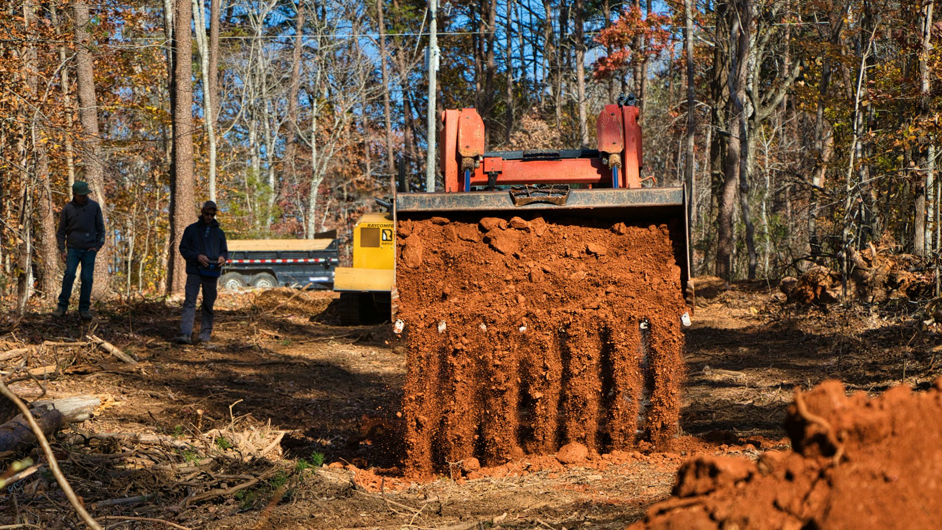 An excavator digging into sandy soil while two crew members look on at a Southwest Florida worksite.