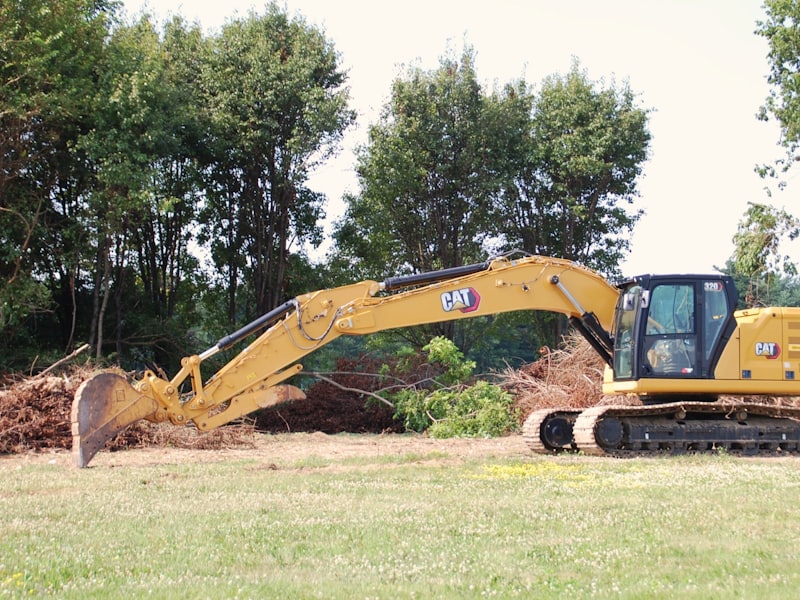 A yellow excavator fitted with a mulching head working along a treeline.